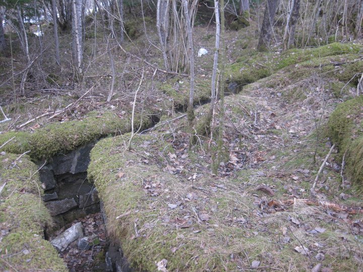 Løpegrav/skyttergrav i stein/betong v. Tøssesvingen. Løpegraven er litt gjenfylt men ellers intakt.