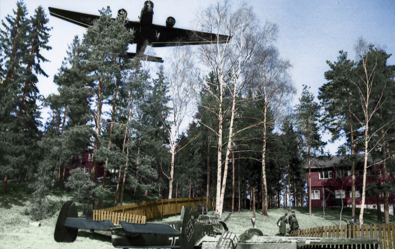 A Messerschmitt 110 has crash landed in the garden of a house during the invasion of Norway. A Junkers JU-52 plane flies over the location. Photo taken by war reporters of the 5th Luftwaffe, April 1940