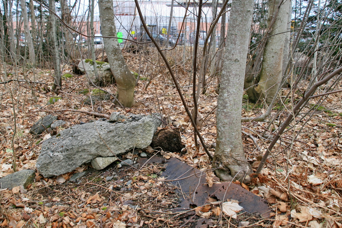 Rusten metallplate, betongbiter og en stor stein, v. utkanten av leir-området.
