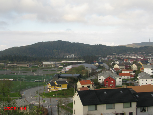 Utsikt østover. Vi ser den relativt nye leilighetsblokken ved Arkavannet i bakgrunnen. Kombi-bunker #6 ligger i fjellskråningen til høyre for blokken 115moh., 1,9km fra Hest. Høyeste topp (Arka) på den fjellryggen er på 174moh.<br />Steinsfjellet(224 moh.) th.